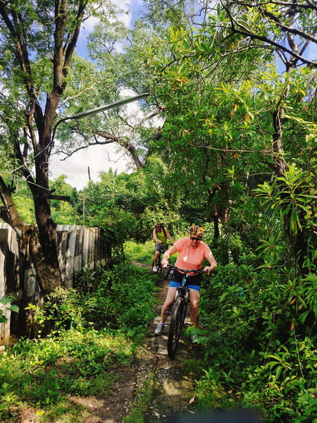 Cyclist navigating through thick jungle vegetation on a narrow dirt trail in Bang Krachao's Green Lung