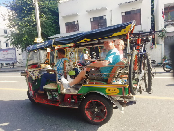 Colourful Tuk Tuk transporting cyclists with their bikes mounted on the back through Bangkok streets