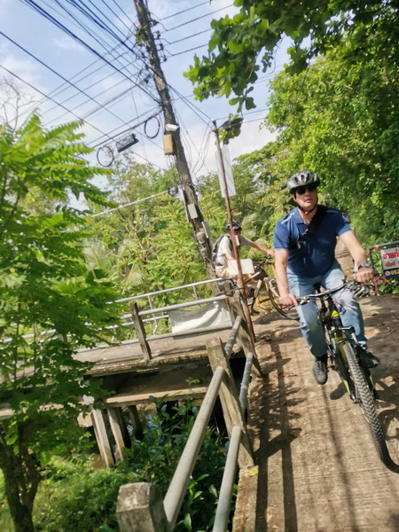 Cyclist riding on a narrow elevated concrete walkway with colourful railings through dense jungle
