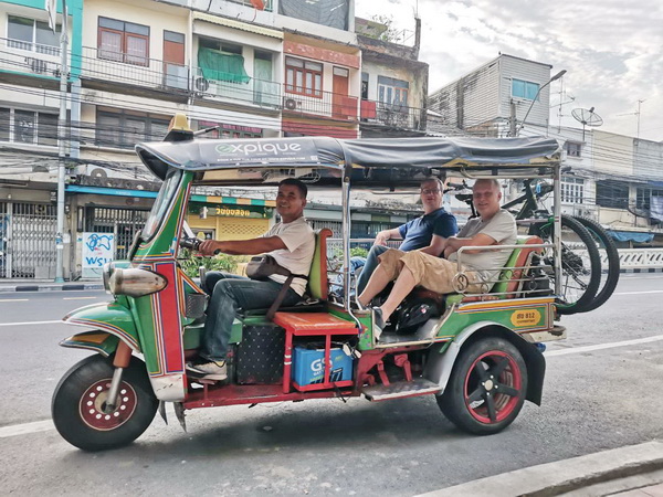 Cyclists being transported in a classic green and red Tuk Tuk with their mountain bikes on the back