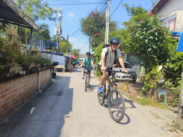 Family cycling together on narrow elevated walkways through dense tropical jungle in Bang Krachao