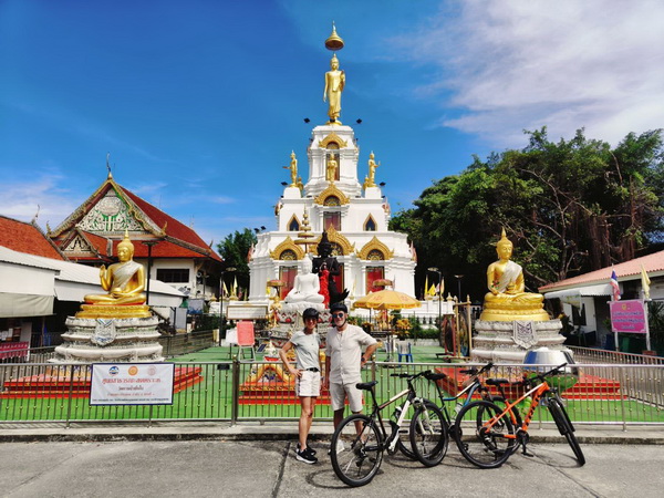 Family posing with their bikes in front of a magnificent white temple with golden Buddha statues and ornate spires