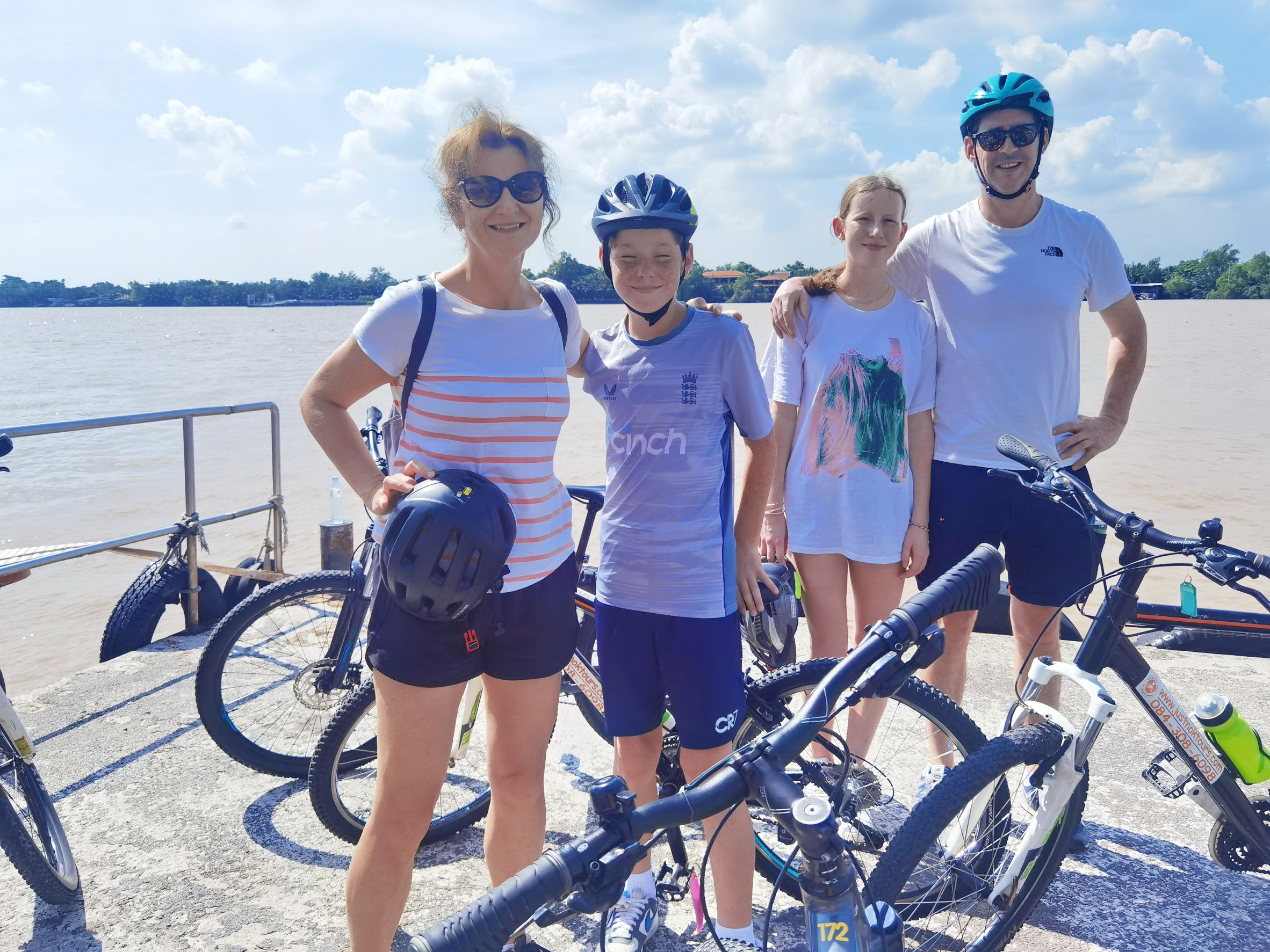 Cyclists waiting at the ferry pier with their mountain bikes, overlooking the calm river surrounded by lush greenery