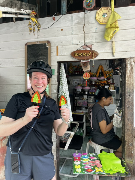 Happy cyclist holding up colorful handmade Thai leaf-shaped craft ornaments outside a local artisan shop
