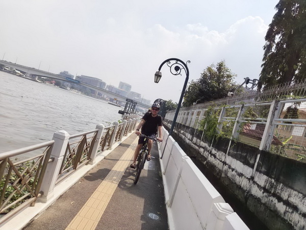 Cyclist riding along the scenic riverside promenade next to the Chao Phraya river