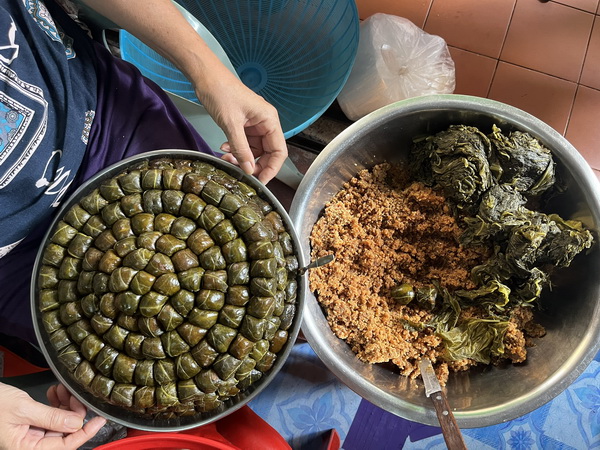 Local vendor preparing traditional Thai sweets wrapped in banana leaves in large metal bowls