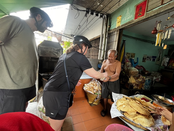Cyclists sampling crispy homemade snacks from a friendly local vendor in his riverside shop