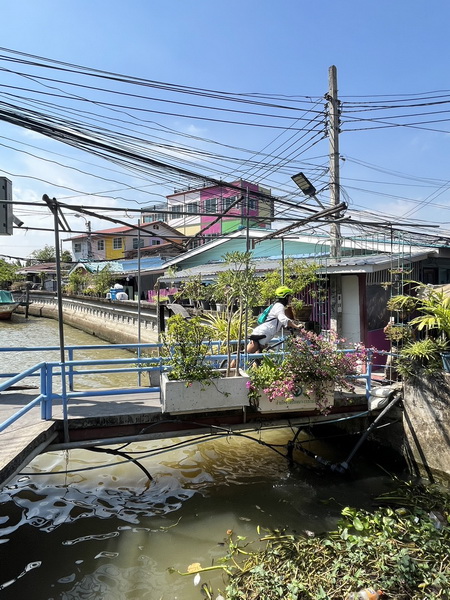 Cyclist crossing a small bridge over a canal in colorful old Bangkok riverside community