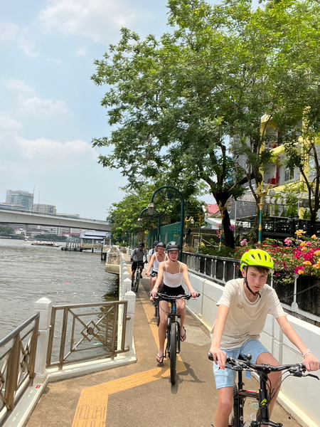 Cycling group riding along the tree-lined riverside promenade with the Chao Phraya river