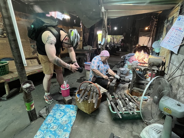 Cyclist watching a local artisan demonstrating the traditional craft of making bronze bowls