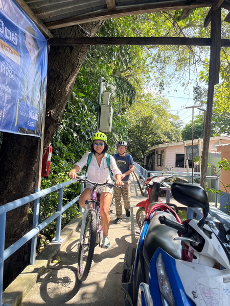 Cyclists navigating narrow walkways and bridges through old Bangkok riverside communities
