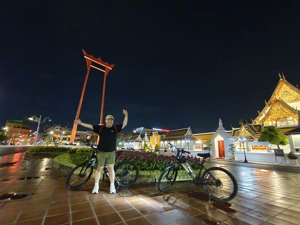 Cyclist celebrating at the Giant Swing with illuminated temple in the background
