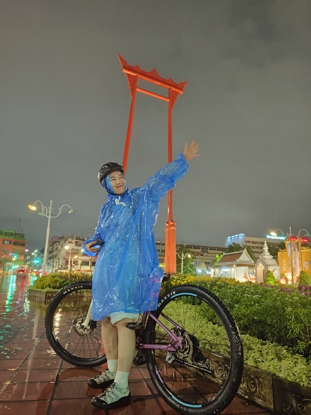 Cyclist in blue rain poncho at the Giant Swing during a rainy evening tour