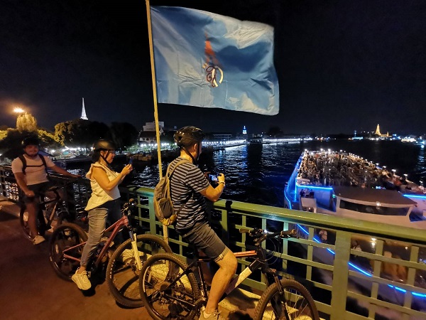 Cyclists on Memorial Bridge overlooking the Chao Phraya river and illuminated Wat Arun