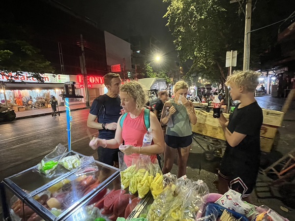 Tour group sampling street food from a night vendor during the Bangkok by Night bike tour