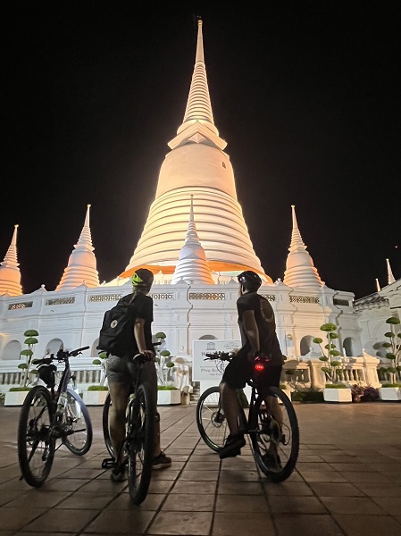 Cyclists admiring the illuminated white spires of Wat Prayurawongsawat temple at night