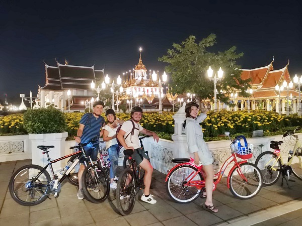 Tour group posing with bicycles in front of the beautifully lit Loha Prasat temple