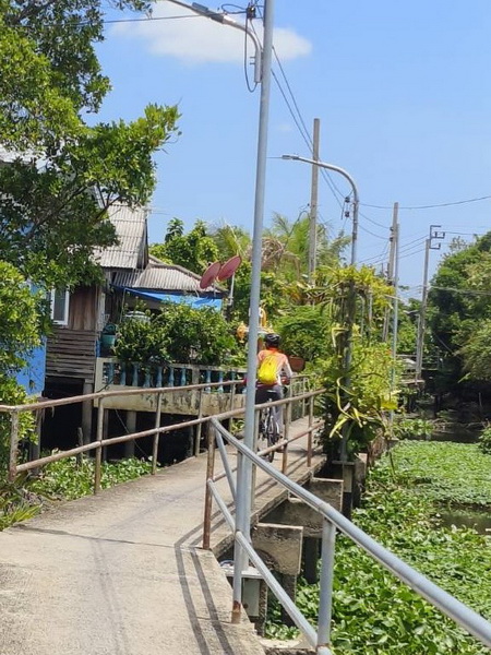 Cyclist riding past traditional Thai stilt houses along elevated walkways in the countryside