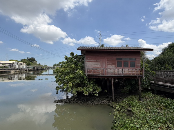 Traditional red wooden Thai house on stilts over a peaceful canal in the Bangkok countryside