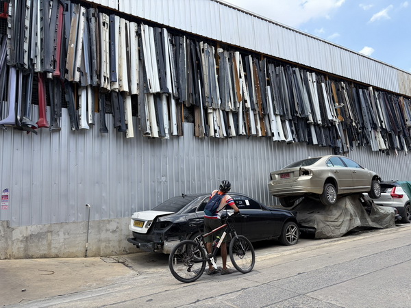 Cyclist stopped beside a unique motor workshop with car doors and bumpers displayed on an industrial wall