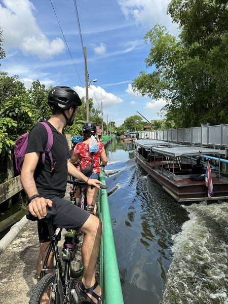 Cyclists watching traditional boats pass through Bangkok canals near floating markets