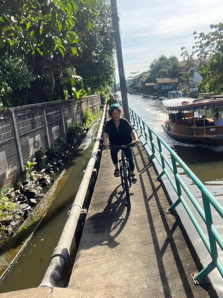 Cyclist riding along narrow elevated walkway beside a canal with a passing boat