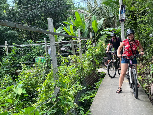 Cyclists riding on narrow elevated walkways through lush greenery along Bangkok canals