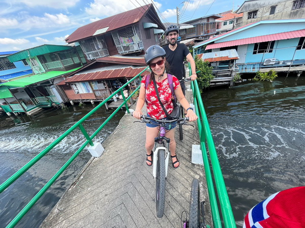 Cyclist crossing a narrow bridge over a canal with colorful stilt houses in the background