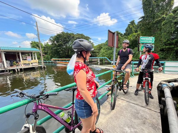 Cyclists gathered at a canal junction with traditional boats passing by