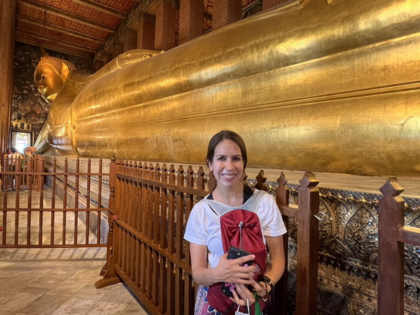 Tourist posing in front of the magnificent golden reclining Buddha at Wat Pho temple in Bangkok