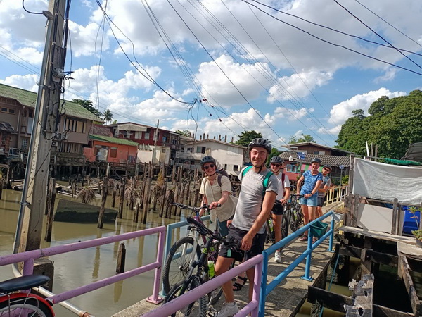 Group of cyclists on a narrow bridge in an old Bangkok waterside community with stilt houses