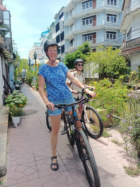 Cyclists riding along a scenic canal pathway with lush greenery and traditional Thai houses