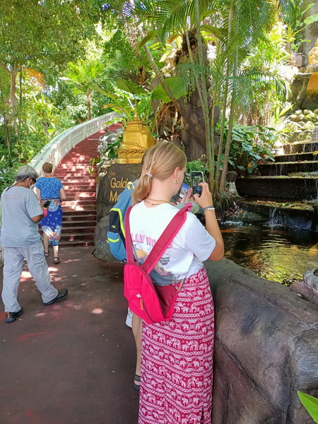 Cyclists at the Golden Mountain temple entrance with lush tropical gardens and waterfall