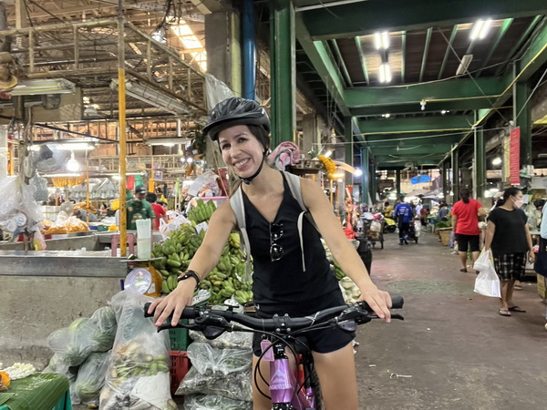 Cyclist smiling while riding through a bustling Bangkok flower and vegetable wholesale market