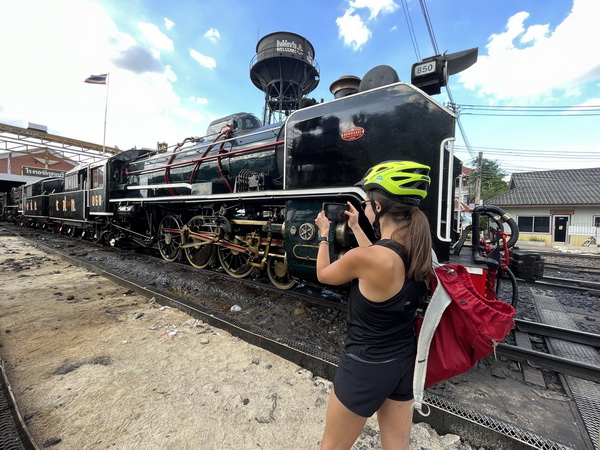 Cyclist taking a photo of the vintage black steam train at the historic Bangkok railway station