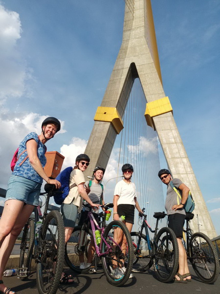 Group of cyclists posing with their bikes beneath the iconic Rama VIII cable-stayed bridge in Bangkok