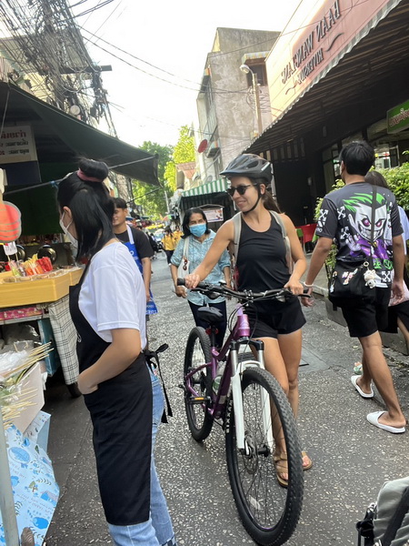 Cyclist walking bike through a narrow alley in a busy Bangkok fresh market with street vendors