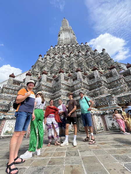 Group of cyclists posing in front of the magnificent prang of Wat Arun temple against a bright blue sky