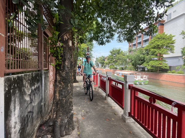 Cyclist riding along a canal-side path with red railings and traditional Thai architecture