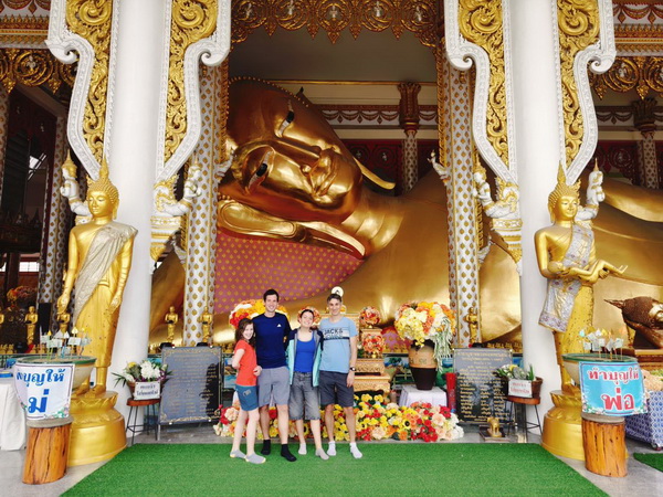 Family standing before a giant golden reclining Buddha inside a temple