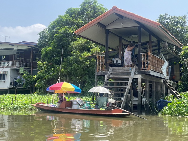 Floating vendor selling goods to a customer at a stilted house on the canal