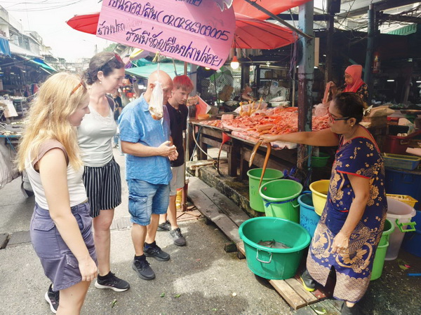 Tour group exploring a local fresh market with a vendor selling seafood