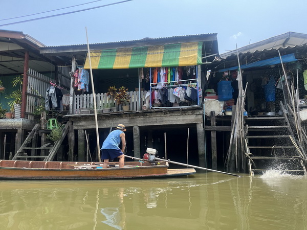 Local man navigating a boat past homes where people wash clothes on the canal