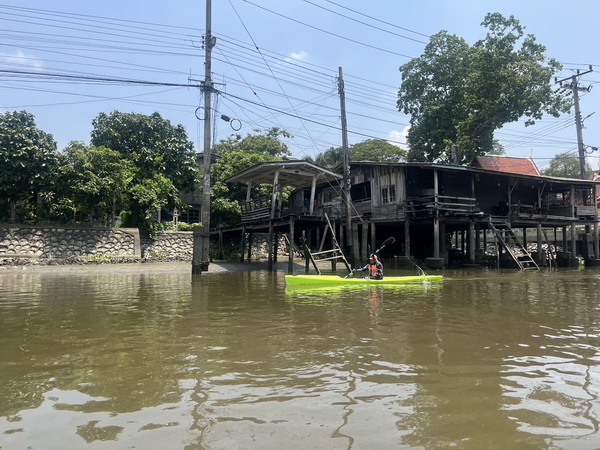 Person kayaking on the canal past traditional wooden stilted houses