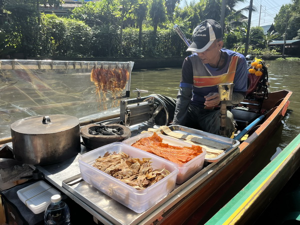 Local vendor cooking and selling food from a small boat on the canal