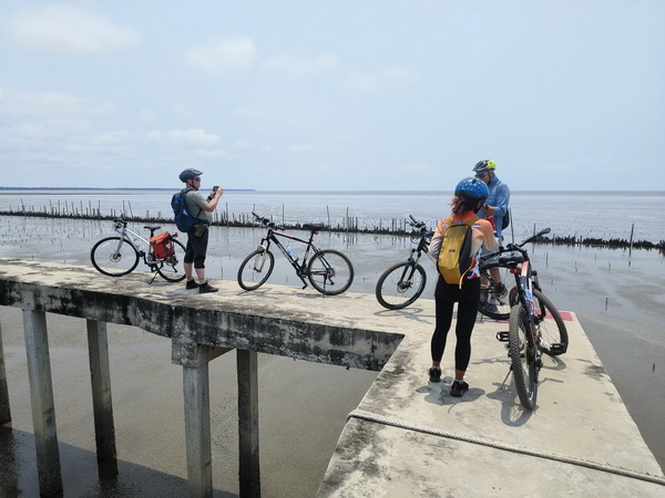 Cyclists with their bikes on a wooden pier at the water's edge overlooking the Gulf of Thailand