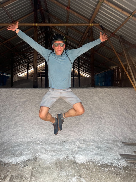 Cyclist jumping for joy inside a traditional Thai salt storage house with a salt floor
