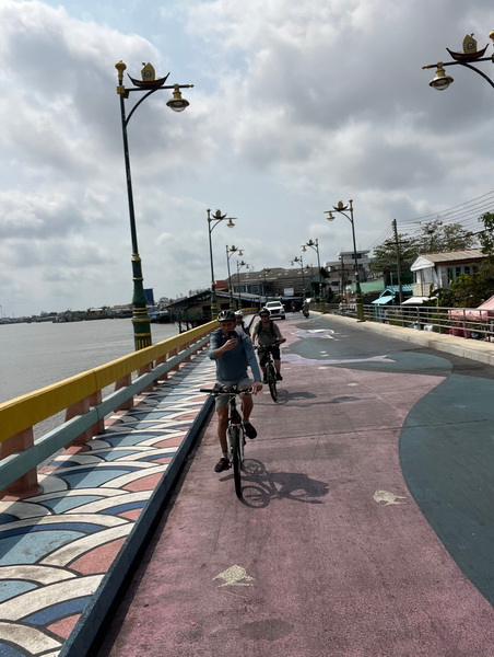 Cyclists riding along a scenic riverside promenade at the mouth of the Ta Chin River