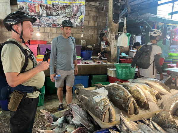 Cyclists exploring a chaotic local fresh fish market with piles of seafood on display