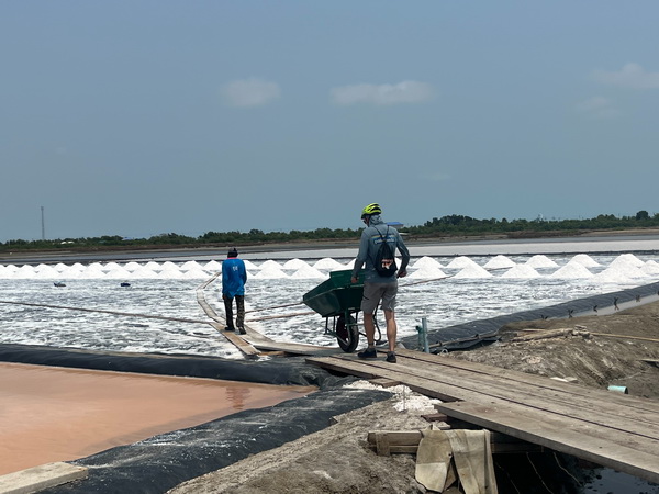 Cyclist with bike standing on wooden walkways between vast white salt pans at the salt farm